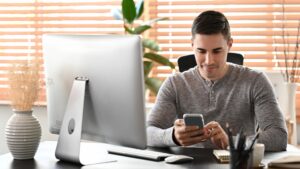 Attractive man sitting at home office and using smart phone.